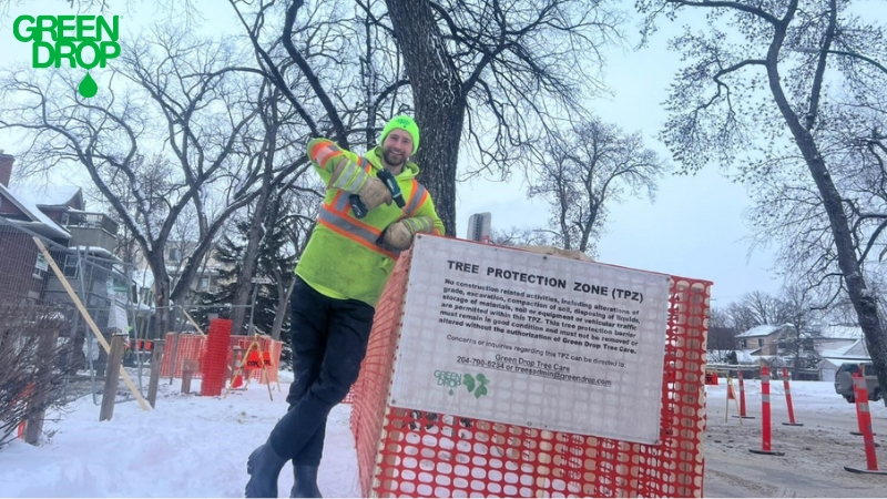 Green Drop employee leaning on a sign during winter