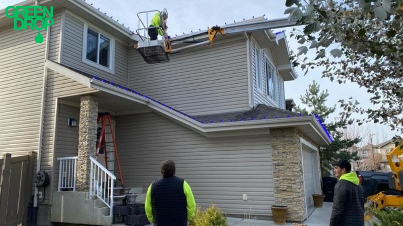 Green Drop workers putting up holiday lights on a house