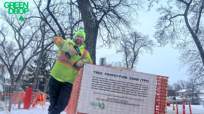 Green Drop worker with a hand drill posing next to a tree protection zone sign