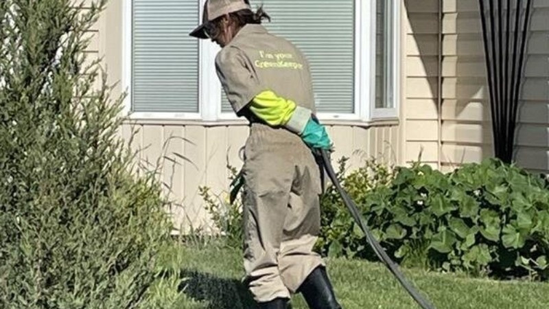 A Green Drop technician applying lawn fertilizer near a residential home. Proper fertilization enhances lawn health.