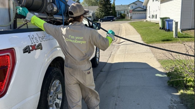 A Green Drop professional setting up lawn care equipment next to a truck in a residential neighborhood.